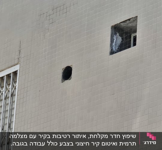 קיר חיצוני של בניין מחופה אריחים עם פתחים וסימני סדקים